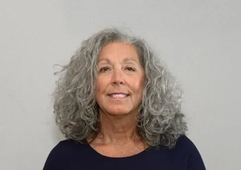 A woman with grey hair is smiling for the camera.