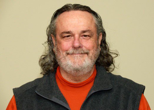 A man with long hair and beard wearing a red shirt.