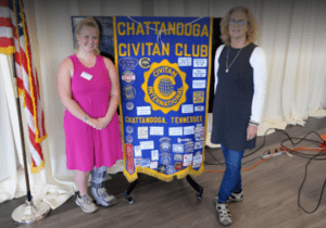 Two women standing next to a banner.